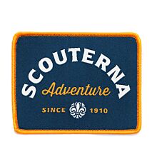 Rektangulärt märke med orange langetterad kant och blå bakgrund med texten Scouterna Adventure Since 1910 och scoutsymbolen på