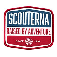 Märke med röd langetterad kant, vit bakgrund och blå detalj med texten Scouterna Raised By Adventure since 1910 och scoutsymbolen på